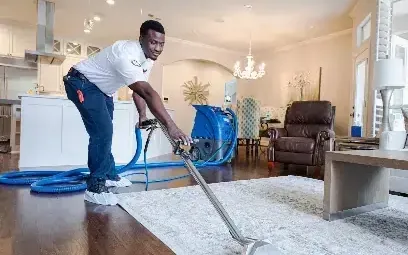 A technician running an extraction wand across a rug in a living room