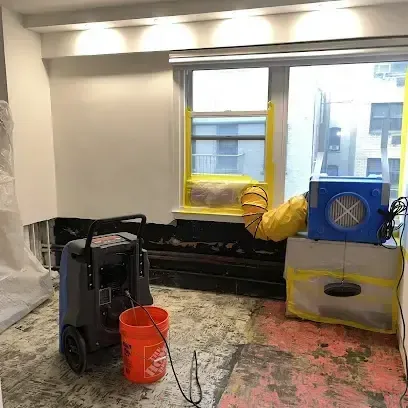 A dehumidifier and an air mover drying a room with the flooring removed after a pipe failure