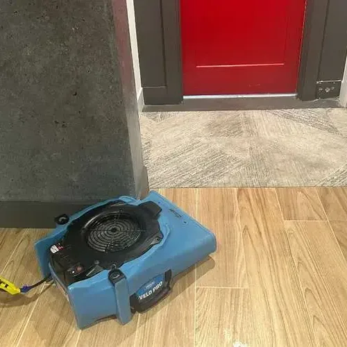 An air mover drying a wood-look tile floor near an open doorway