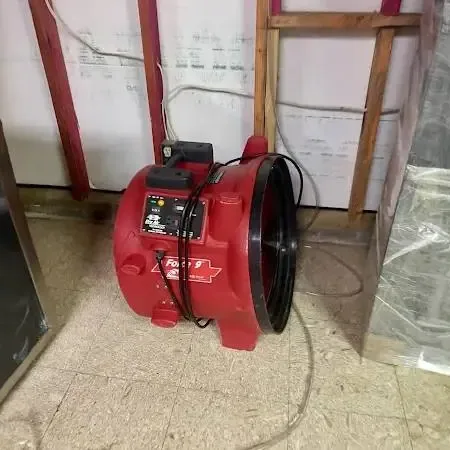 A red air mover drying a room with the lower wall opened and plastic sheeting hung after cleanup