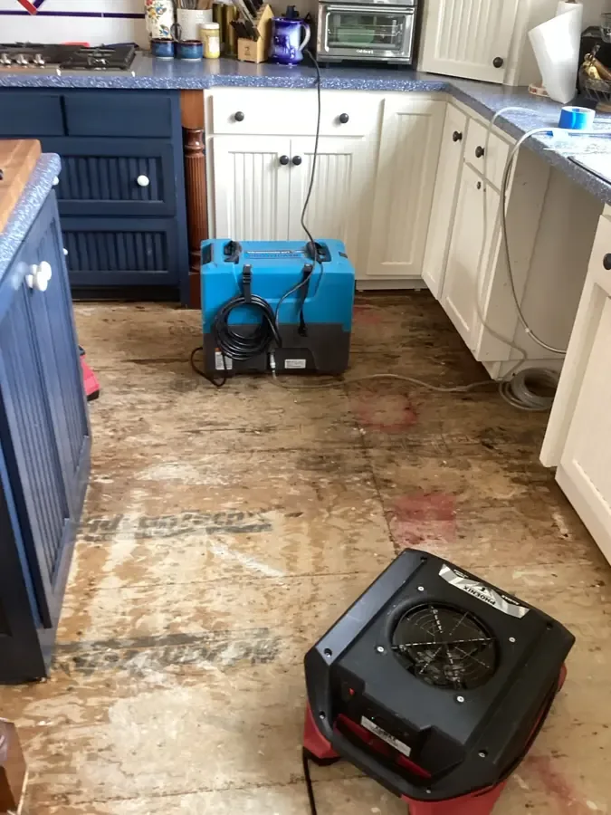 A dehumidifier and air mover drying a kitchen floor after the flooring was pulled up