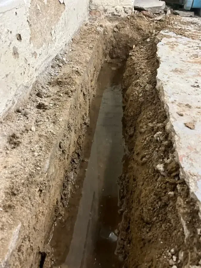 A trench cut into a concrete slab floor to reach a leaking pipe below