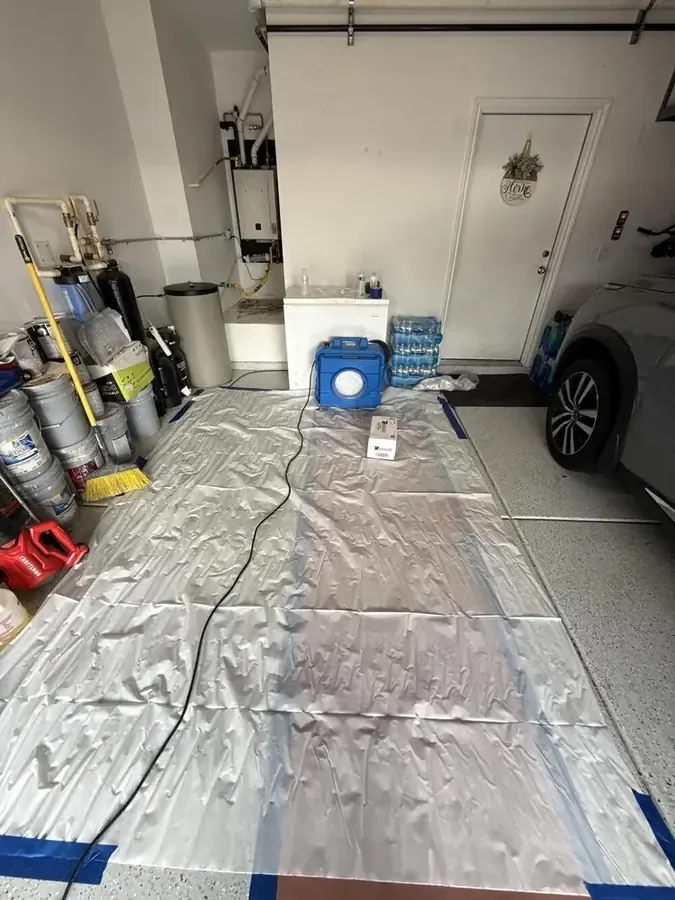 Plastic sheeting laid over a garage floor with drying equipment set up after storm water got in