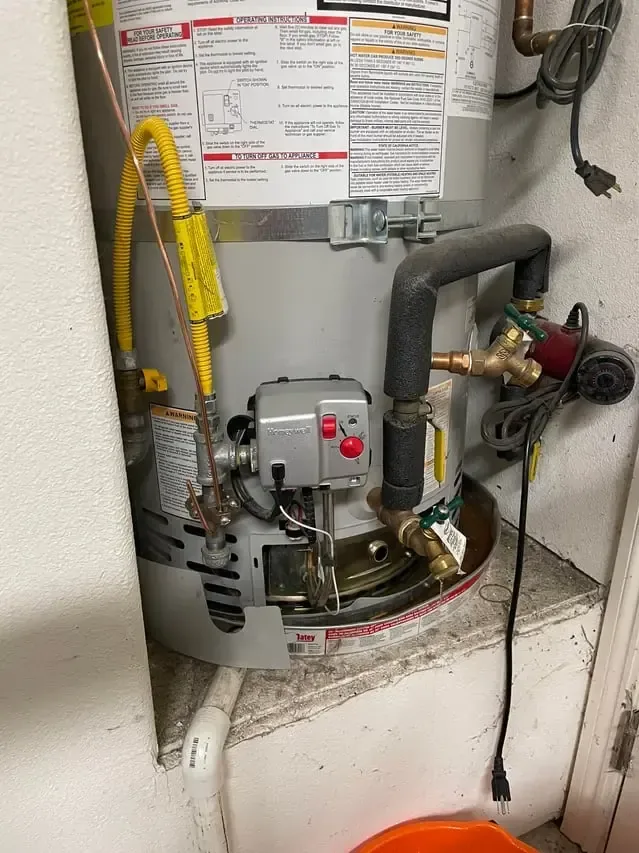 A gas water heater with a bucket at its base catching water from a leak